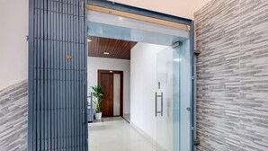 A hallway with a glass door, a potted plant, and a wooden door in the background. - Deluxe With Twin Bed Hotelmbansal Residency (Bhubaneshwar)