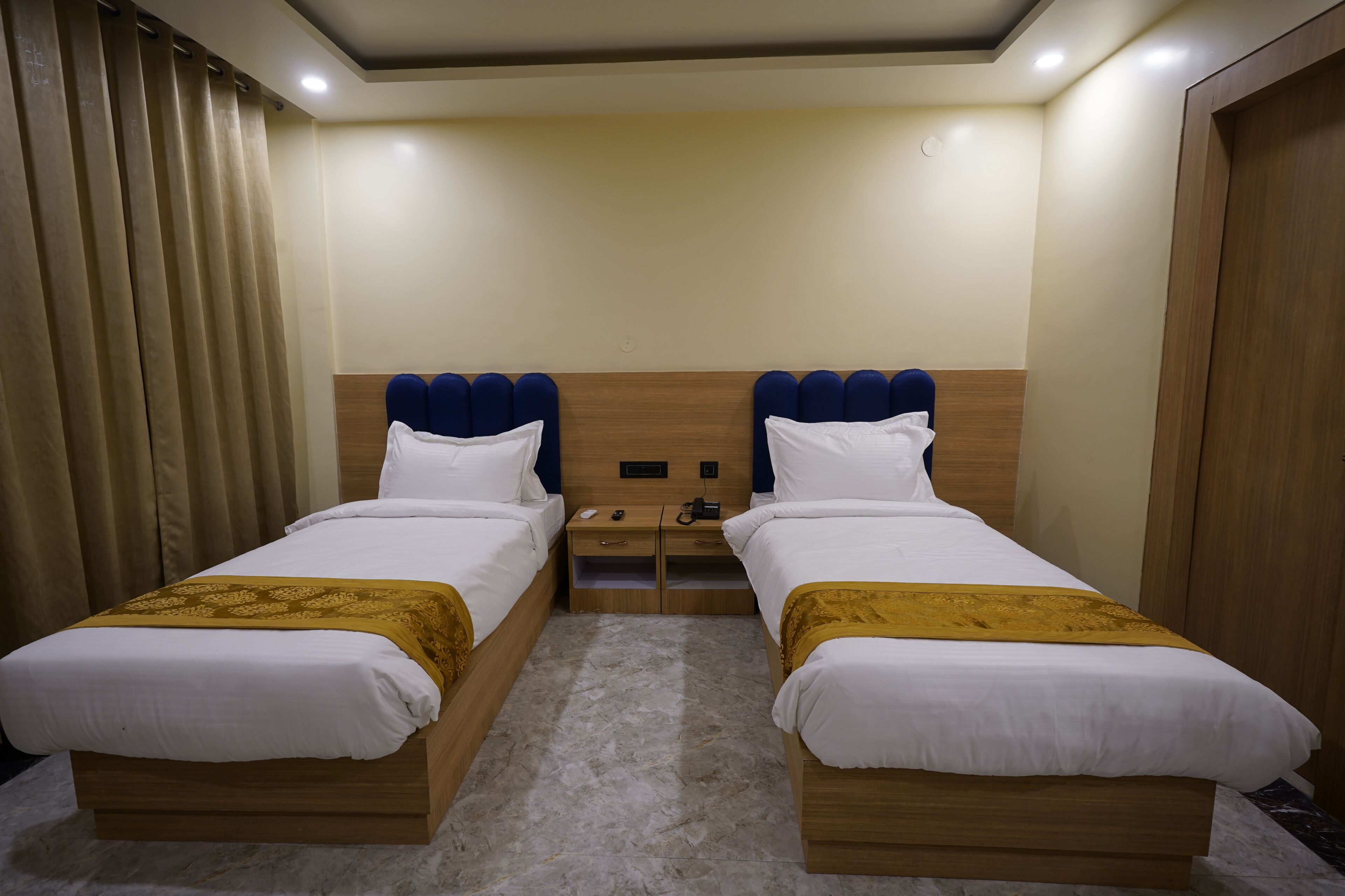 Une chambre d’hôtel avec deux lits, une tête de lit en bois, une table de chevet et un rideau.