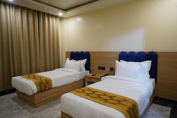 A hotel room with two beds, a wooden headboard, a nightstand, and a curtain. - PS Marriott Hotel (Danapur)