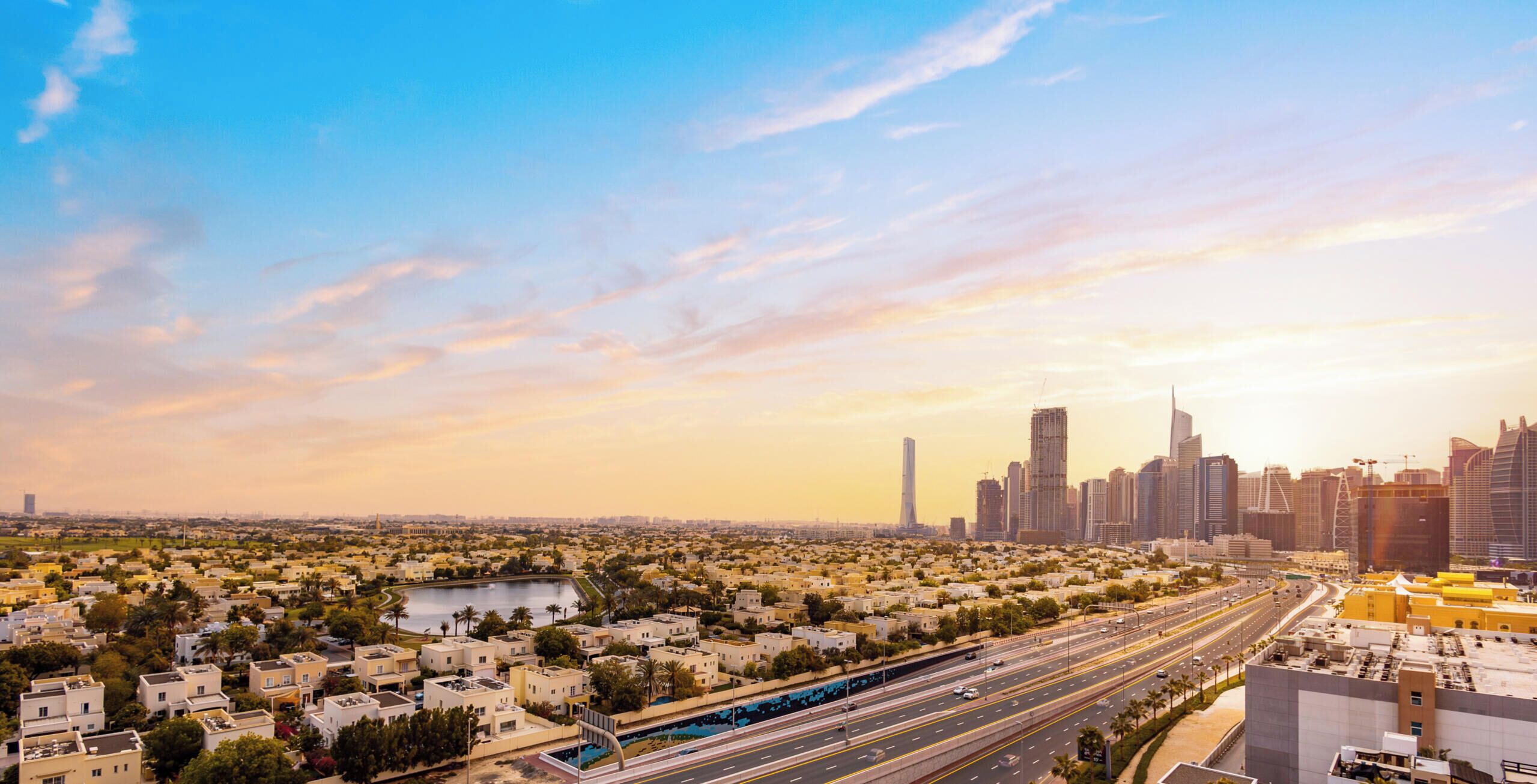 A cityscape with a mix of residential and commercial buildings, a highway, and a clear sky.