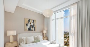 A modern hotel room with a large window, a bed with white linens, two bedside tables with lamps, and a piece of abstract art on the wall. - LUX  The Banyan Tree Suite (Dubai)