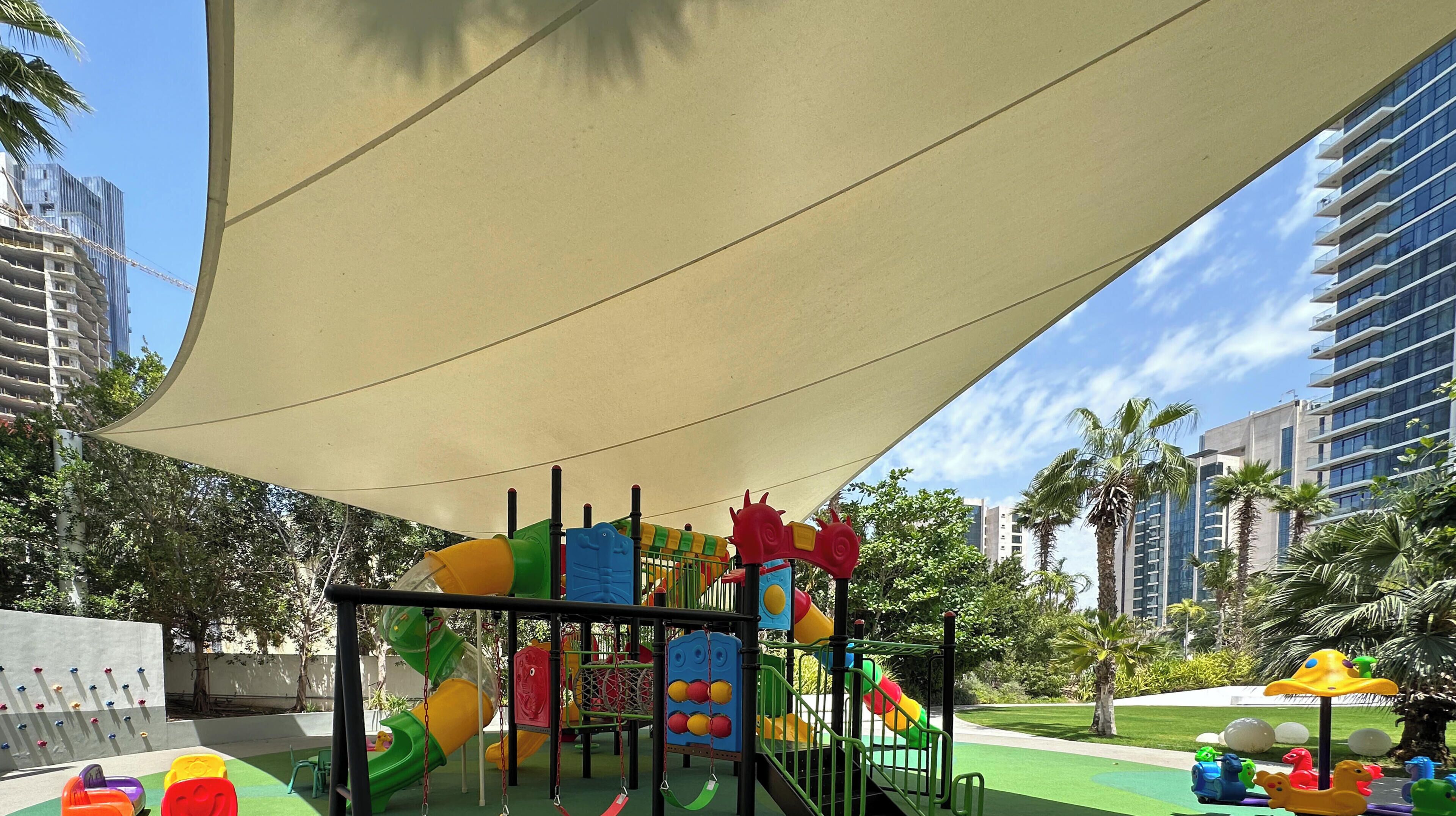 Ein Spielplatz mit Rutschen und Klettergerüsten, umgeben von Palmen und modernen Gebäuden.