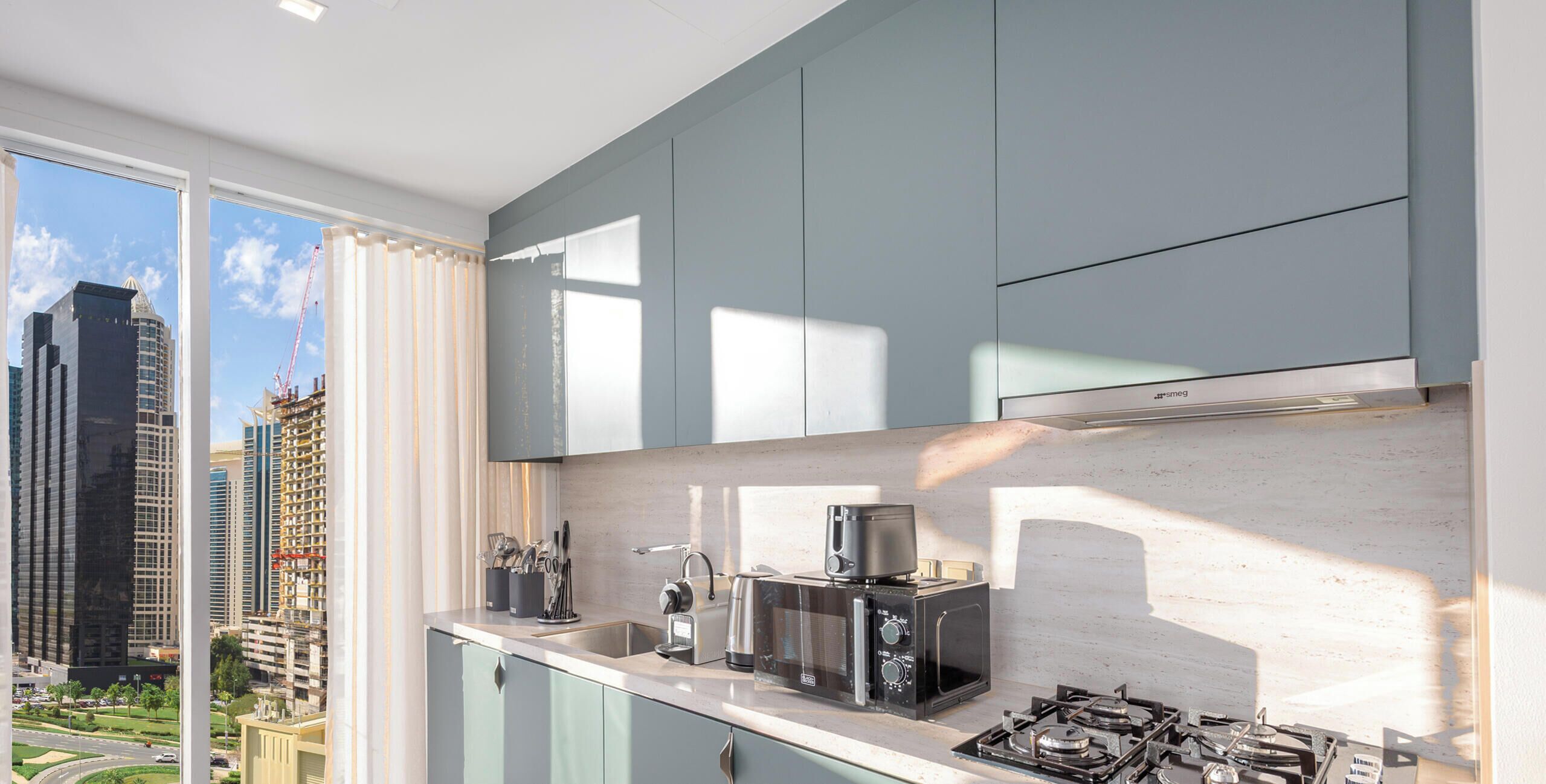 Une cuisine moderne avec vue sur la ville, équipée d’une cuisinière à gaz, d’une machine à café et d’un four à micro-ondes.
