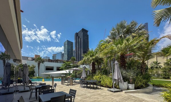 A rooftop pool area with outdoor seating, palm trees, and a city skyline in the background. - LUX  The Banyan Tree Suite (Dubai)