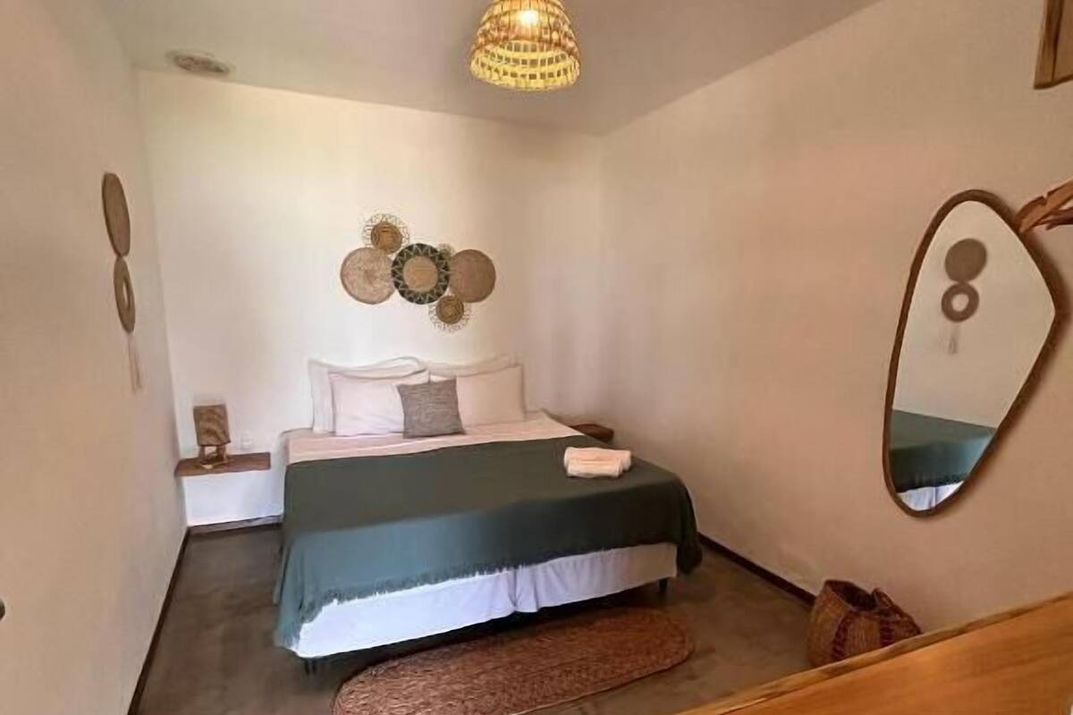 Un dormitorio con una cama, un aparador de madera, un espejo y una lámpara colgante.