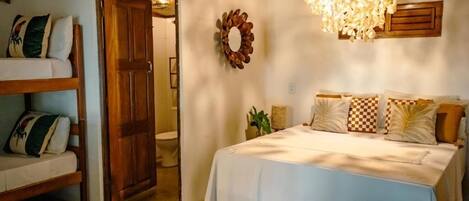 A bedroom with a bed, a wooden door, a wall-mounted air conditioner, a chandelier, and a decorative wall piece.
