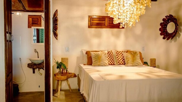 A bedroom with a bed, bedside tables, a hanging light fixture, a mirror, and a wall-mounted shelf. - Cabaré du Vento (Cruz)