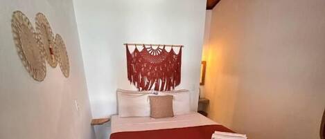Un dormitorio con una cama, una colcha roja, un cabecero de madera, una lámpara colgante y una alfombra estampada.