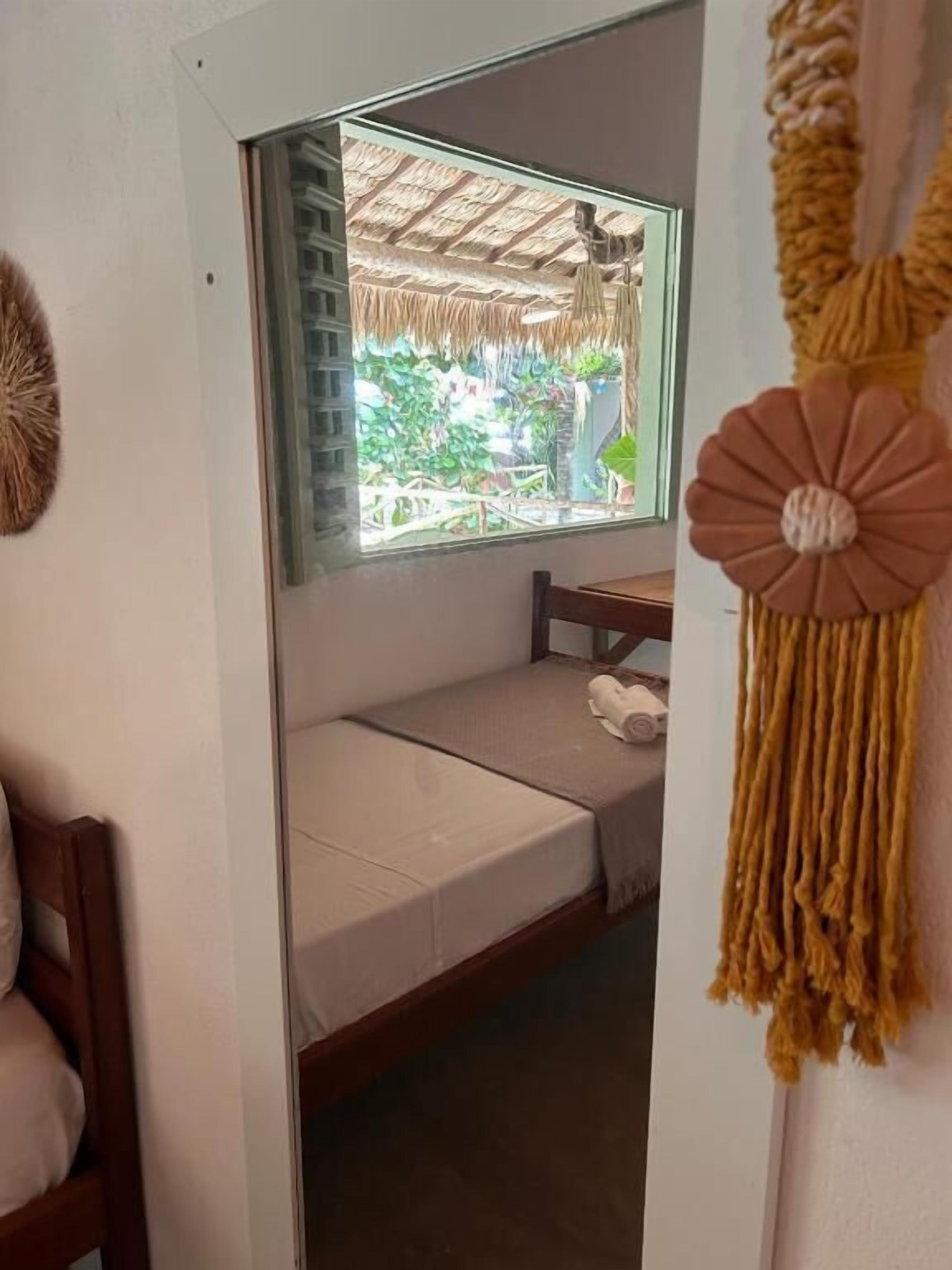A room with a bed, a window with a view of greenery, and a macrame wall hanging.
