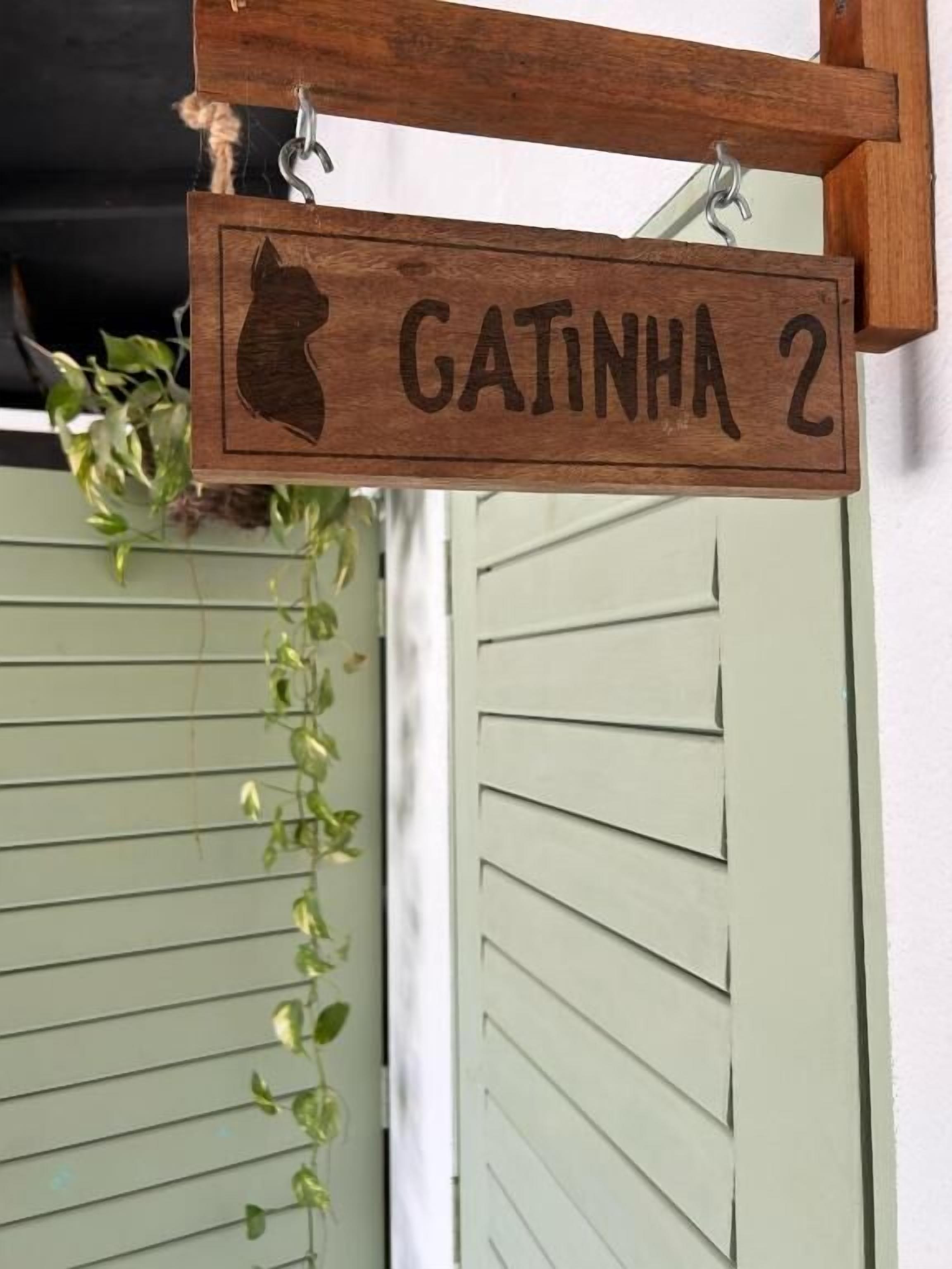A wooden sign with a cat silhouette and the text 'CATINHA 2' mounted on a wall.