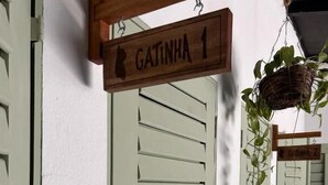 A door with a sign reading 'GATINHA 1' and a hanging basket with green plants. - Cabaré du Vento (Cruz)