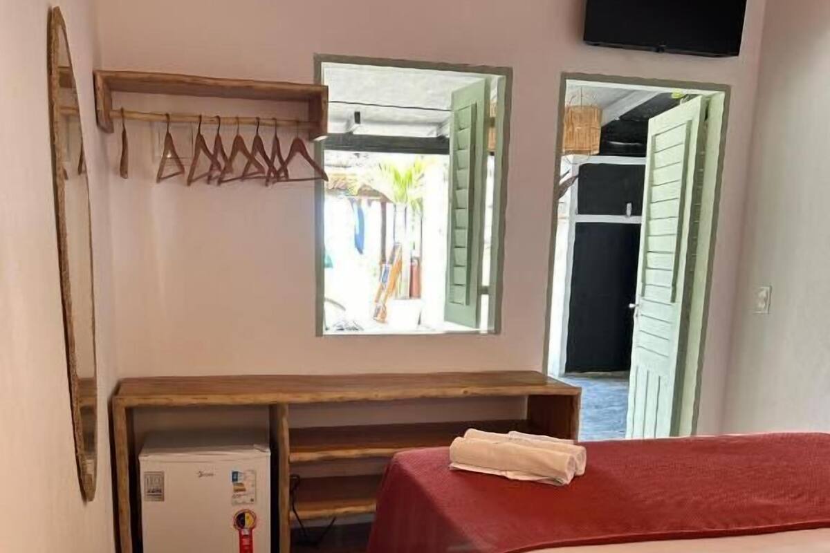 Un dormitorio con cama, televisión, espejo, armario y un refrigerador pequeño.