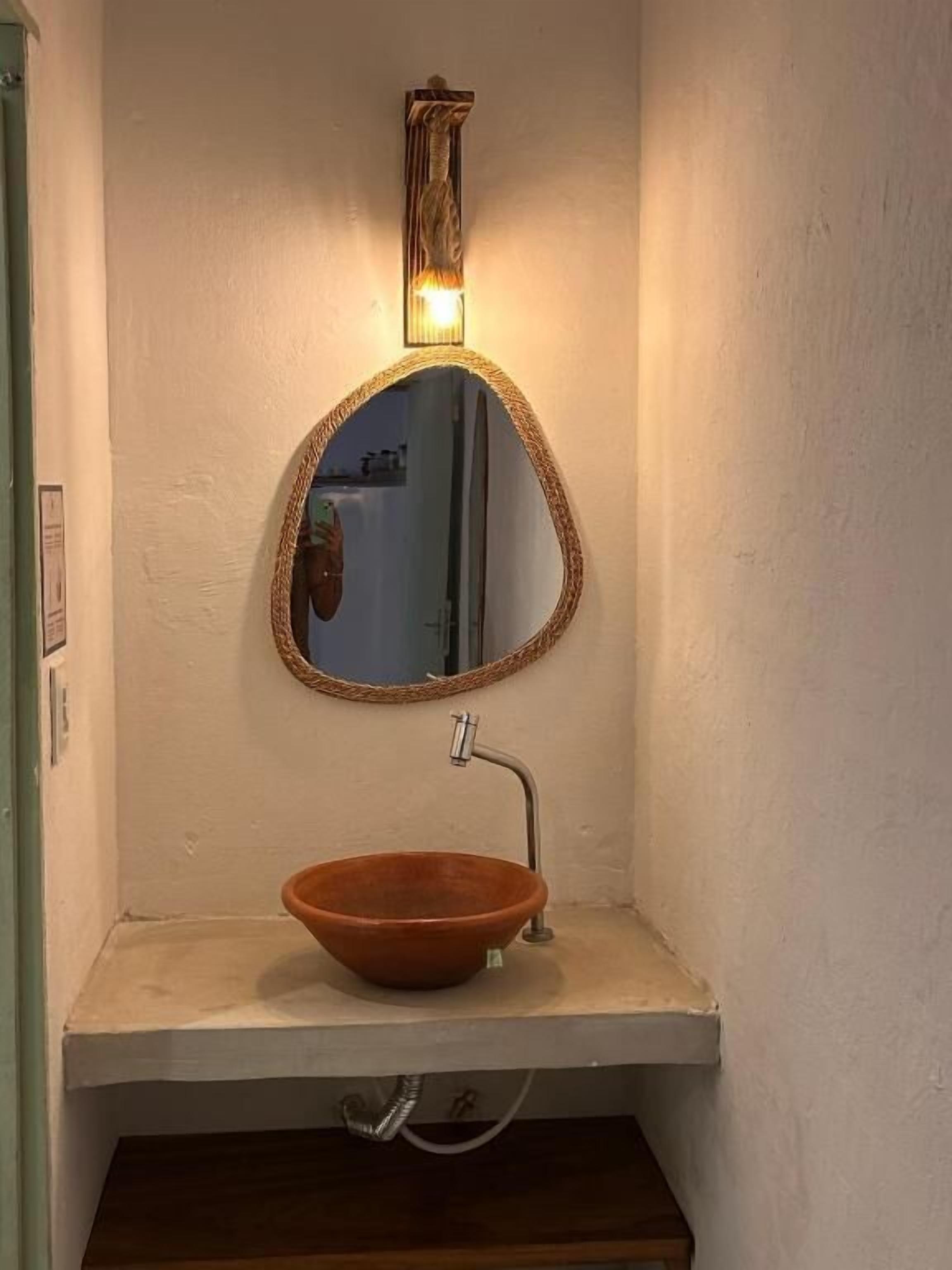 A bathroom with a round mirror, a bowl sink, and a wall-mounted light fixture.