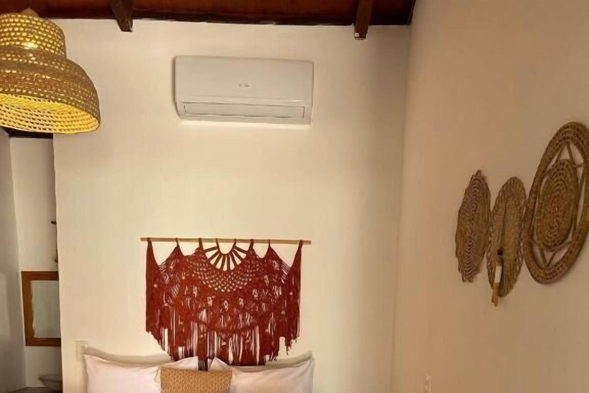 Una cama con una manta roja, almohadas blancas y un cabecero decorativo.