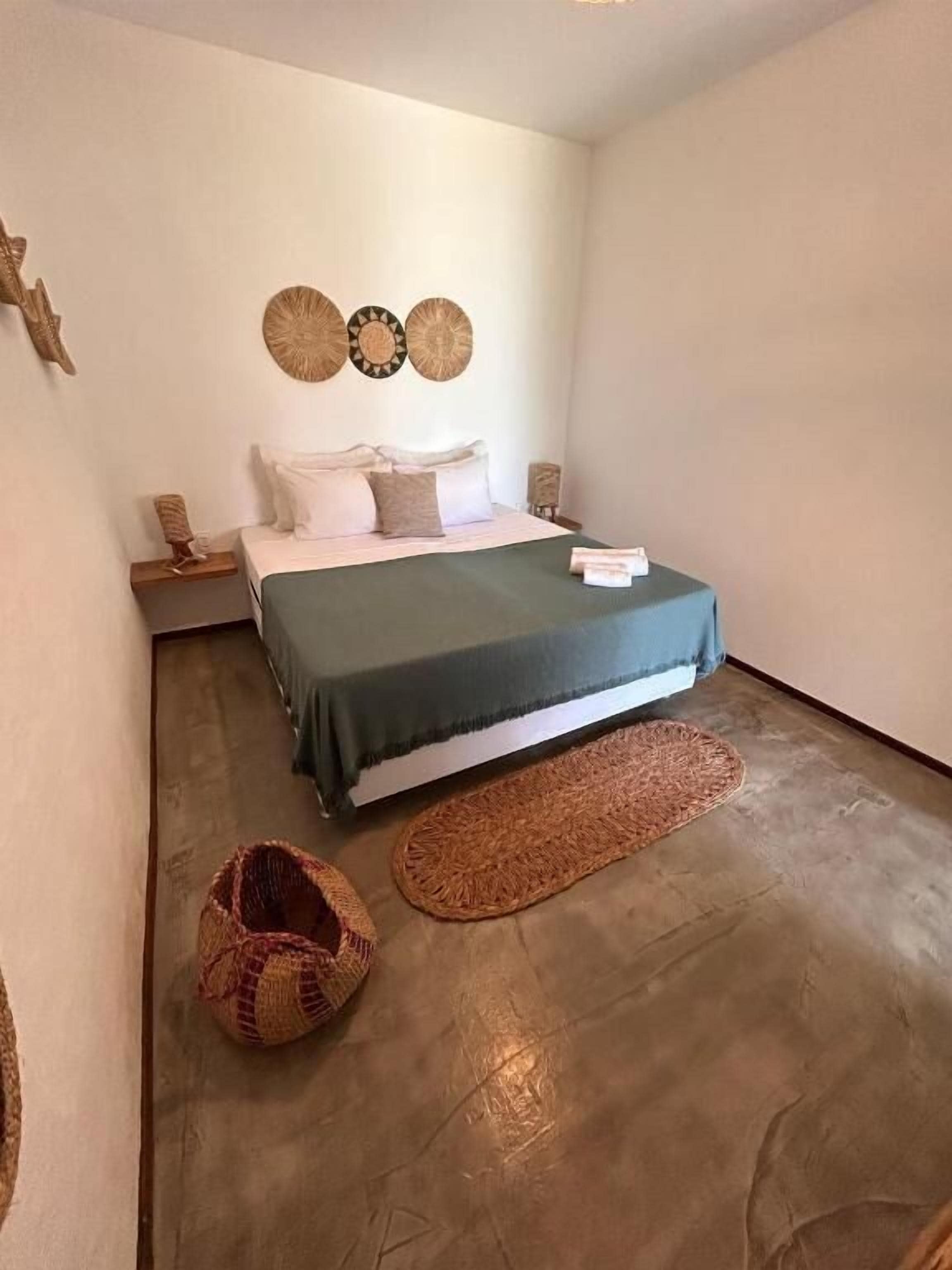 A bedroom with a bed, a bedside table, a wall-mounted clock, and a woven rug.