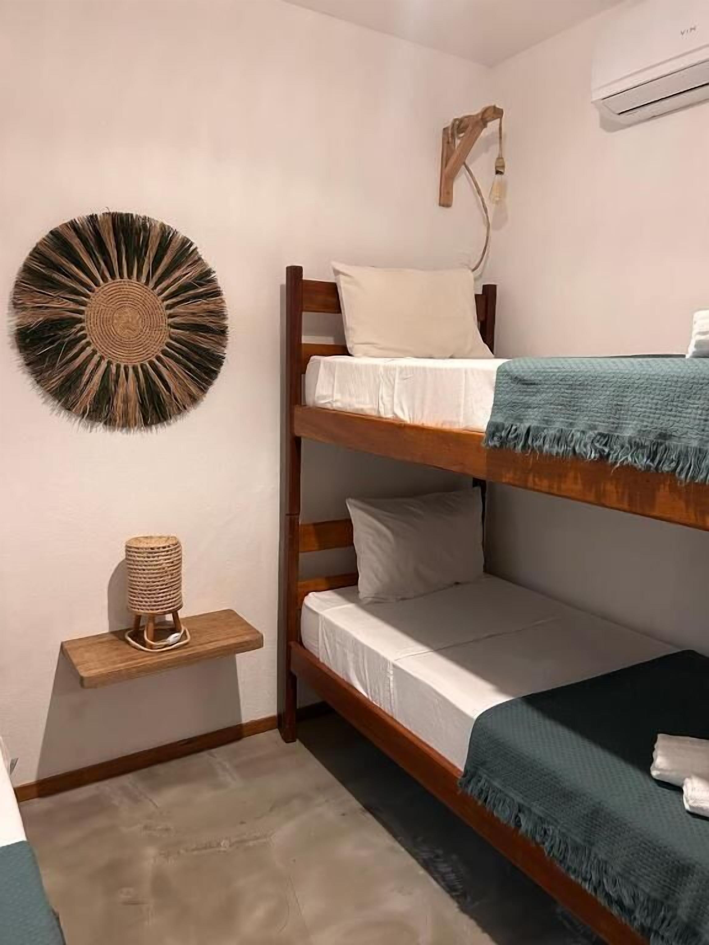 Habitación con literas, aire acondicionado de pared, adorno de pared tejido y un pequeño estante con un objeto tejido.