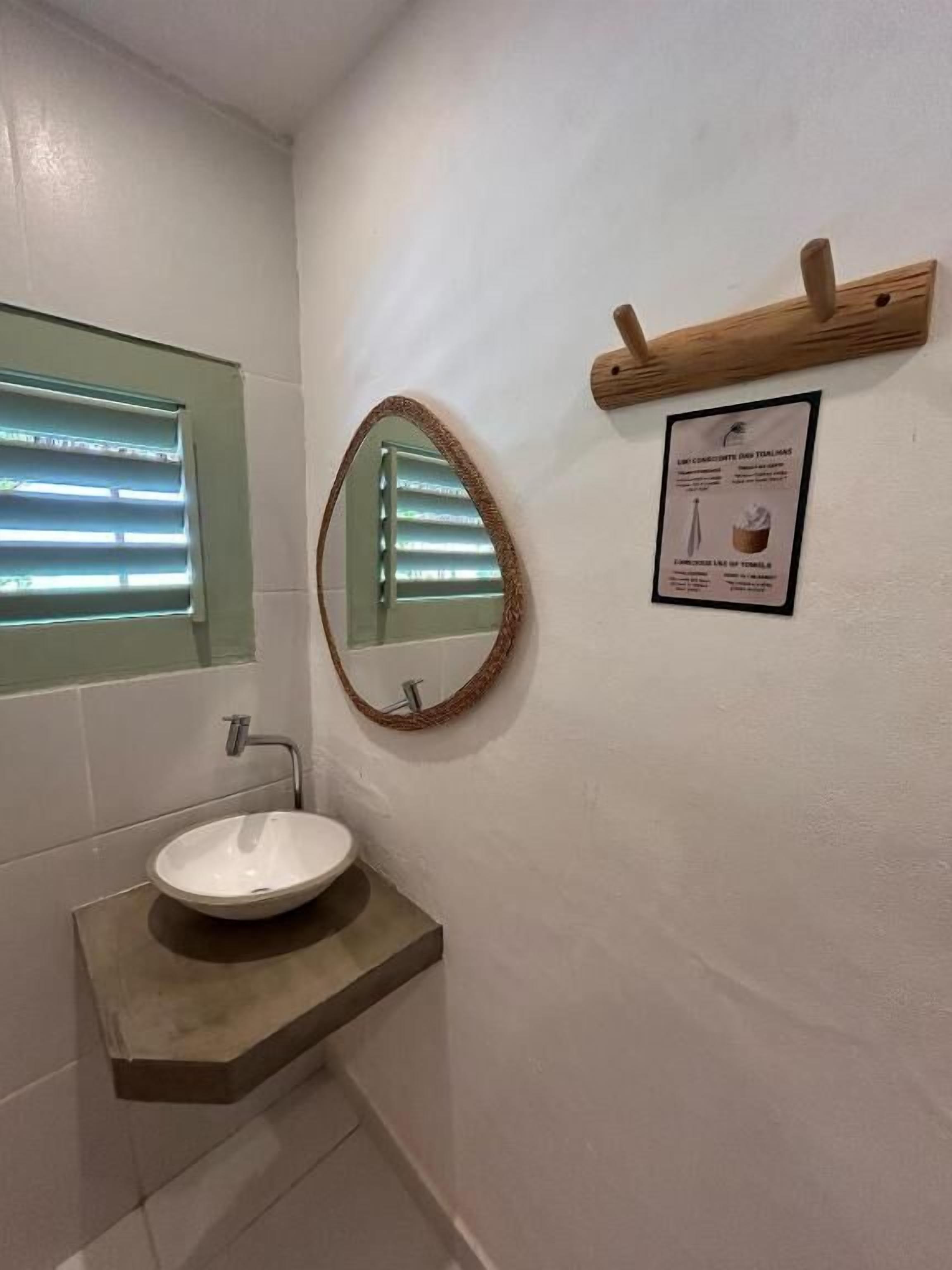 A bathroom with a white sink, a mirror, and a wooden shelf.