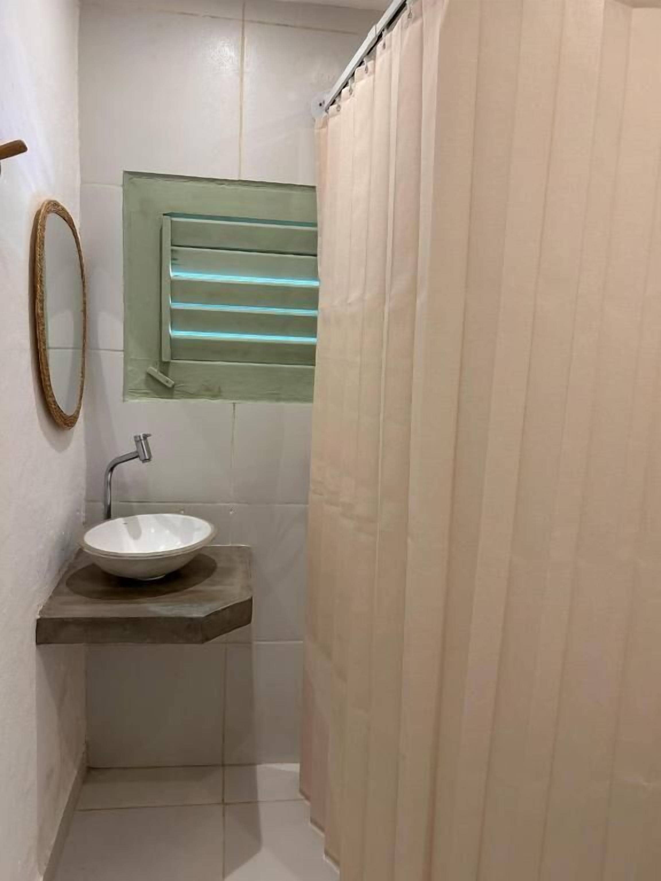 A bathroom with a white sink, a mirror, and a window with blinds.
