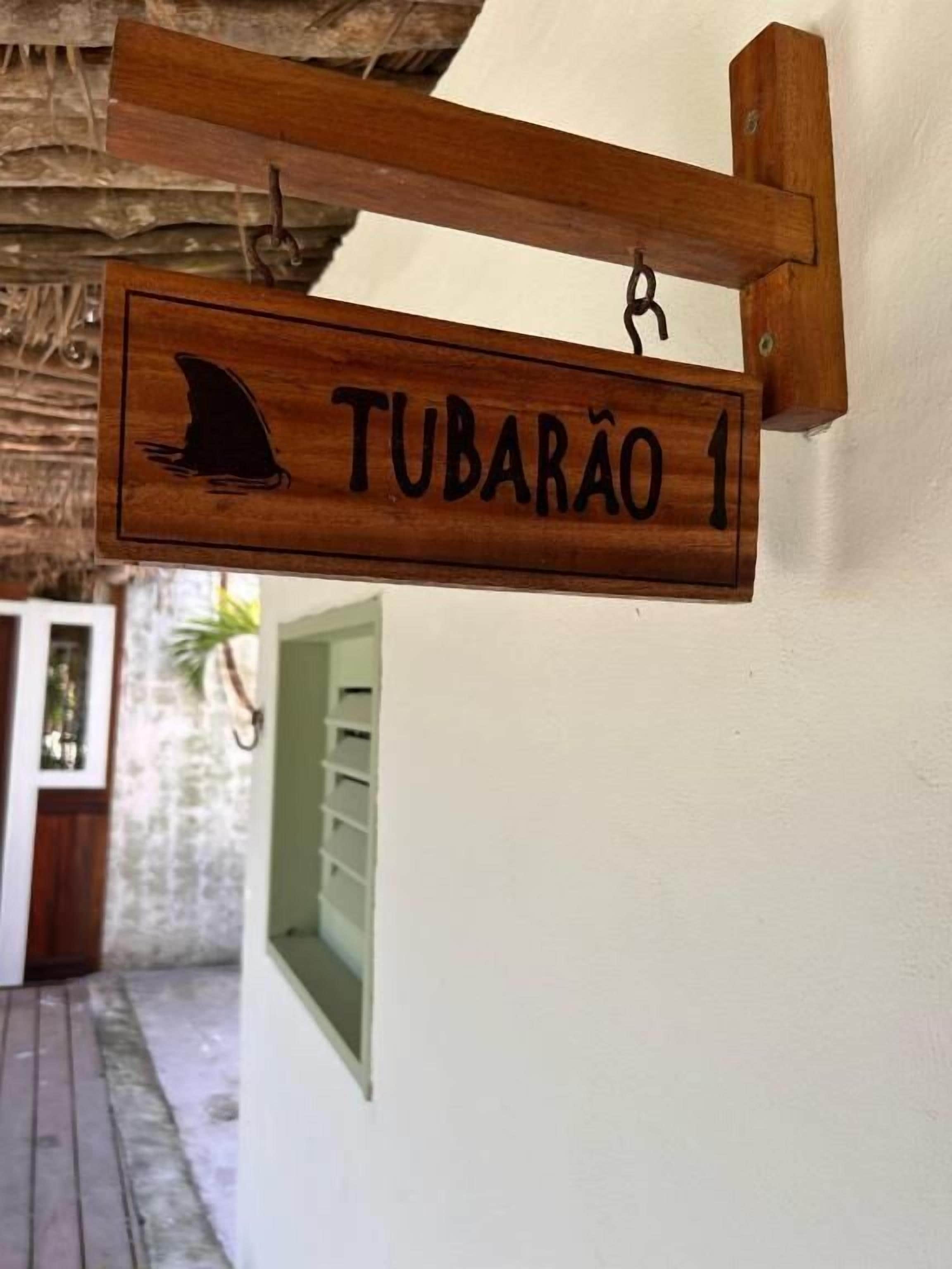 Une enseigne en bois représentant la silhouette d’un requin et portant le nom « TUBARÃO 1 », fixée à un mur.