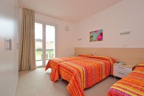 Ein Hotelzimmer mit zwei Betten, einer Schiebetür zum Balkon, einem Nachttisch und einer Wandleuchte.