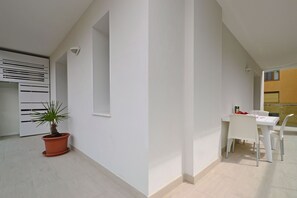 Ein modernes, minimalistisches Zimmer mit einem weißen Tisch und Stühlen, einer Topfpflanze und einem weißen Schrank mit horizontalen Linien.