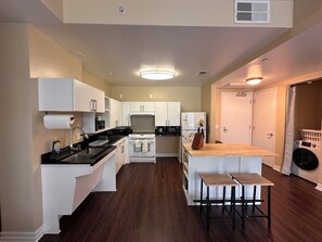 A modern kitchen with white cabinets, a black countertop, and a wooden island with stools. - KTown 2BR - Parking, Pool, Walk to Metro (Los Angeles)