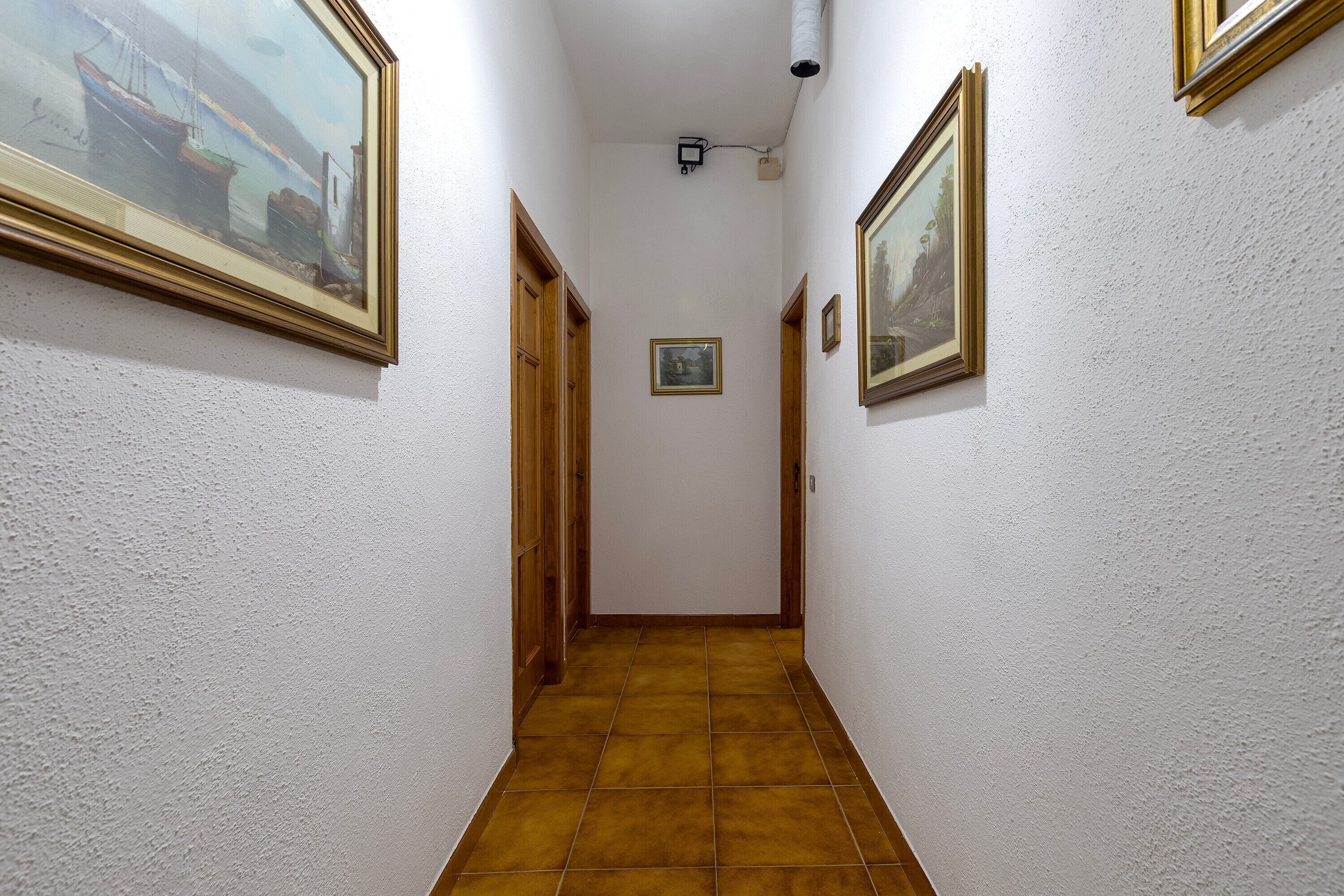 Un pasillo con suelo de baldosas, paredes blancas y cuadros enmarcados.