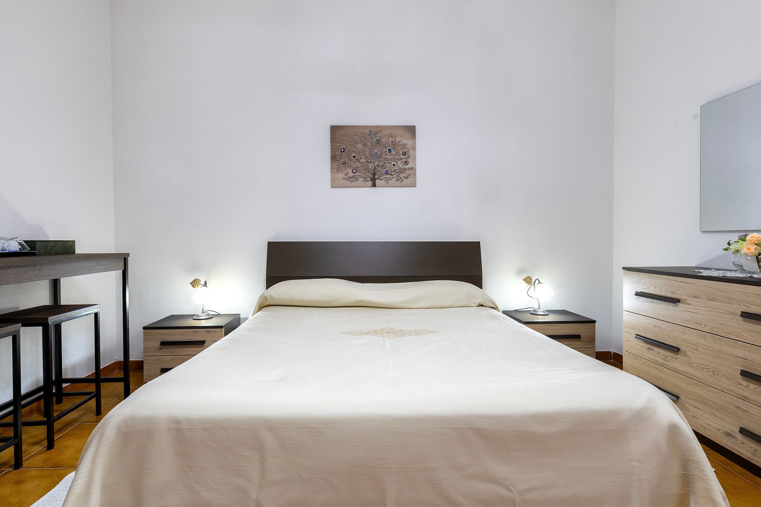 Ein ordentlich eingerichtetes Schlafzimmer mit einem Bett, Nachttischen, einem Schreibtisch und einer Kommode.