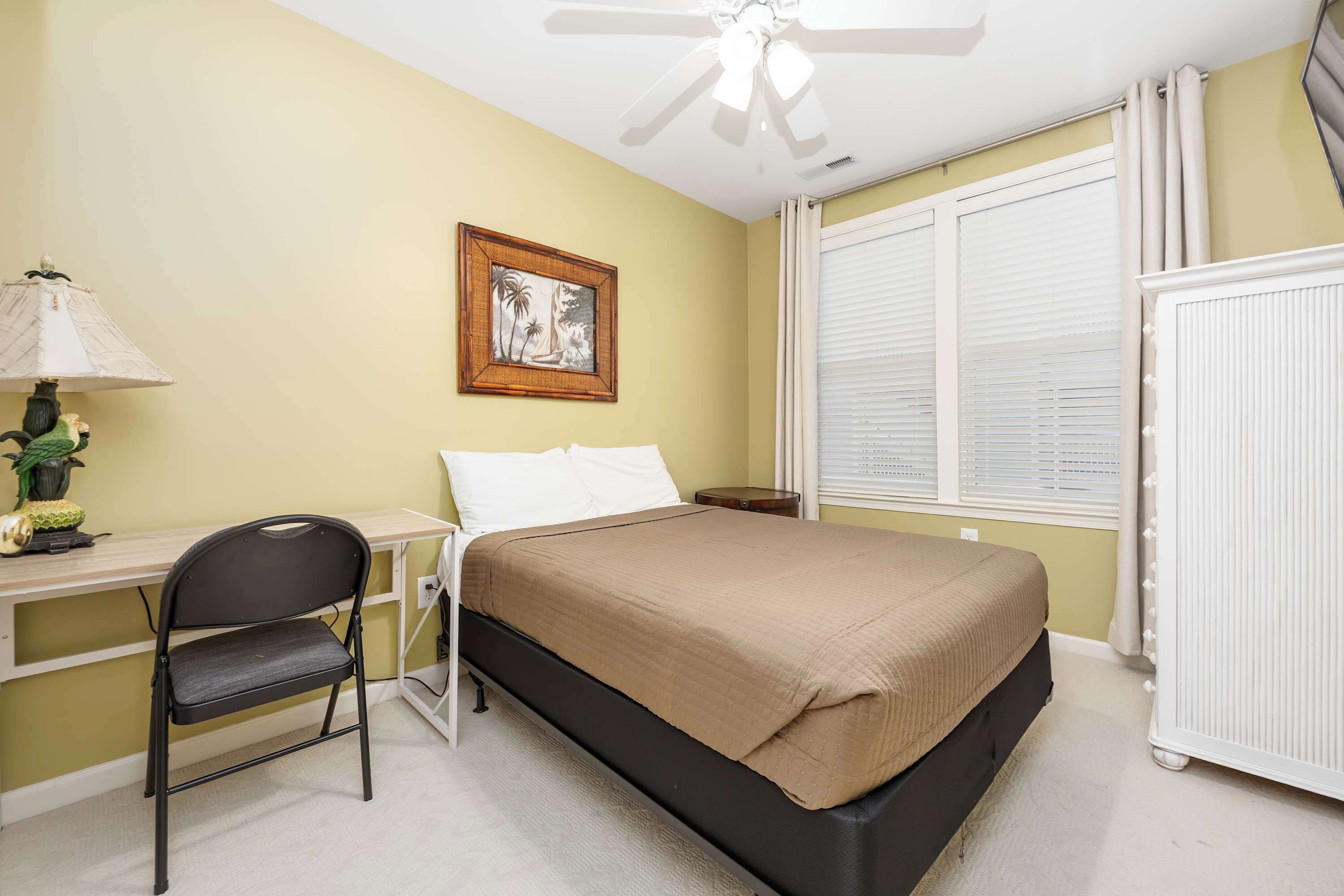 A bedroom with a bed, desk, chair, and a ceiling fan.