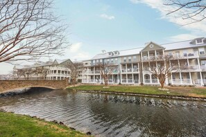 A waterfront hotel with multiple balconies, a stone bridge, and a calm river. - Sunset Island - 5 Brs/ Sleeps 12 / 2 pools (Ocean City)