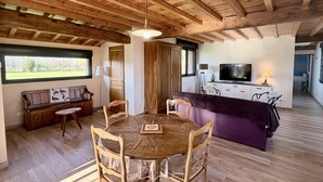 Een gezellig interieur met een houten plafond, een eethoek met een ronde tafel en stoelen, een bank en een keuken met een televisie.