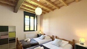 Een slaapkamer met twee bedden, een houten plafond, een raam en een nachtkastje met een lamp.