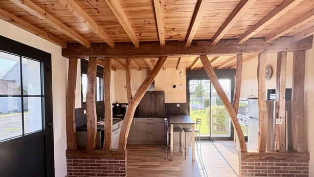 Een keuken met zichtbare houten balken, een bakstenen open haard en een uitzicht door grote ramen.