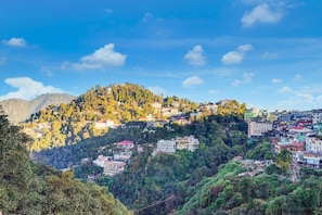 Un village perché sur une colline, avec des bâtiments, une forêt dense et une montagne en arrière-plan.