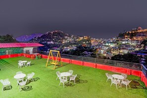 Una terraza en la azotea con mesas y sillas, un columpio y vistas de un paisaje urbano nocturno.