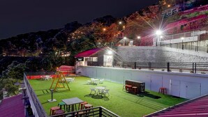 A rooftop terrace with a grassy area, tables, chairs, and a swing set. - Townhouse Mall Road Near Library Chowk (Dehradun)