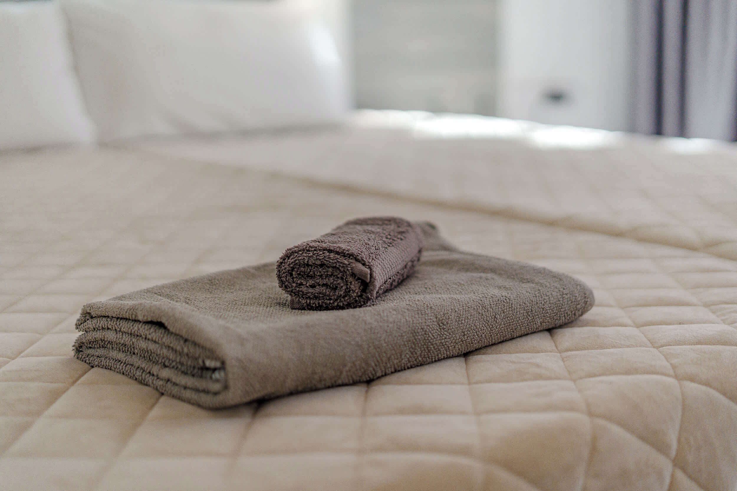 A neatly made bed with a rolled towel on top, a quilted bedspread, and white pillows.