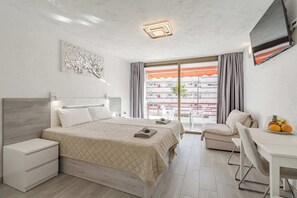 Habitación de hotel con cama, escritorio, silla, televisión y balcón con vistas.