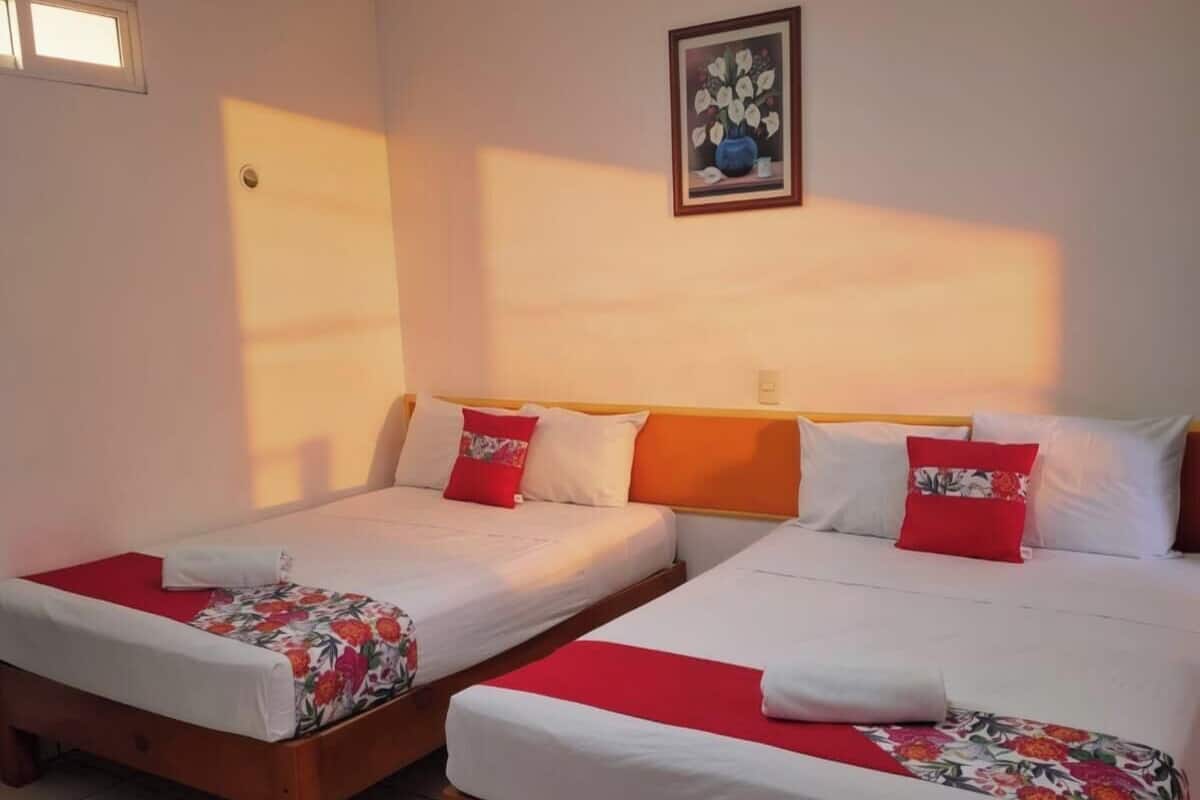 A hotel room with two single beds, a large window, a painting on the wall, and a tiled floor.