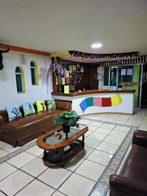 A reception area with a curved counter, a brown leather sofa, a wooden coffee table, and a tiled floor. - Hotel México (Chetumal)