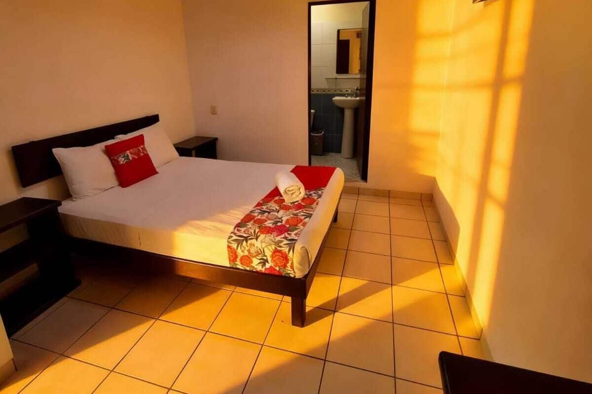 A hotel room with a bed, a nightstand, a TV mounted on the wall, and a bathroom visible through an open door.