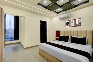 Una habitación de hotel moderna con una cama grande, techo con iluminación empotrada, equipo de aire acondicionado y una obra de arte en la pared.