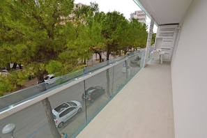 A balcony with a glass railing overlooking a street with cars and trees. - Relaxing Stay in a Beachside Flat (Lignano Sabbiadoro)