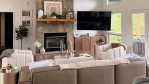 A modern living room with a stone fireplace, a large sectional sofa, a flat-screen TV, and a unique chandelier. - Newly renovated 4B, 4BA in Deerfield (LaFollette)