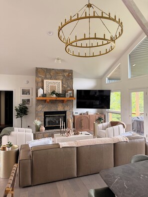 A modern living room with a stone fireplace, a large sectional sofa, a television, and a chandelier. - Newly renovated 4B, 4BA in Deerfield - Interior pics will be posted soon! (LaFollette)