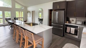 A spacious kitchen with a large island, dark cabinetry, stainless steel appliances, and a dining area with wooden chairs. - Newly renovated 4B, 4BA in Deerfield (LaFollette)