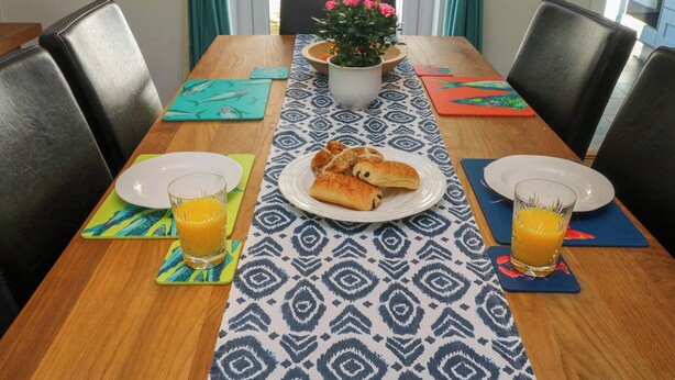 Een eettafel met borden, glazen sinaasappelsap en een bloemenstuk als decoratie.
