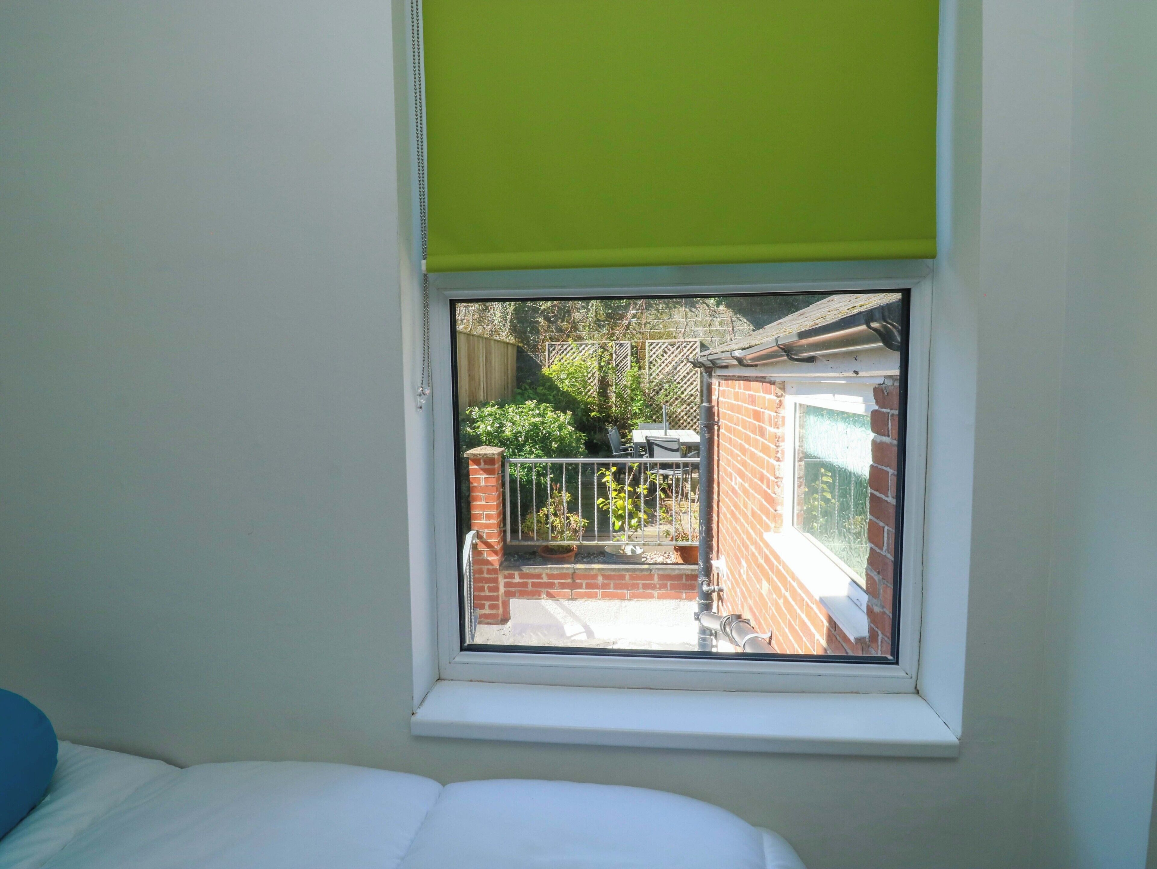 A bedroom with a window overlooking a brick wall and a garden.