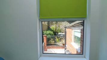 A bedroom with a window overlooking a brick wall and a garden.