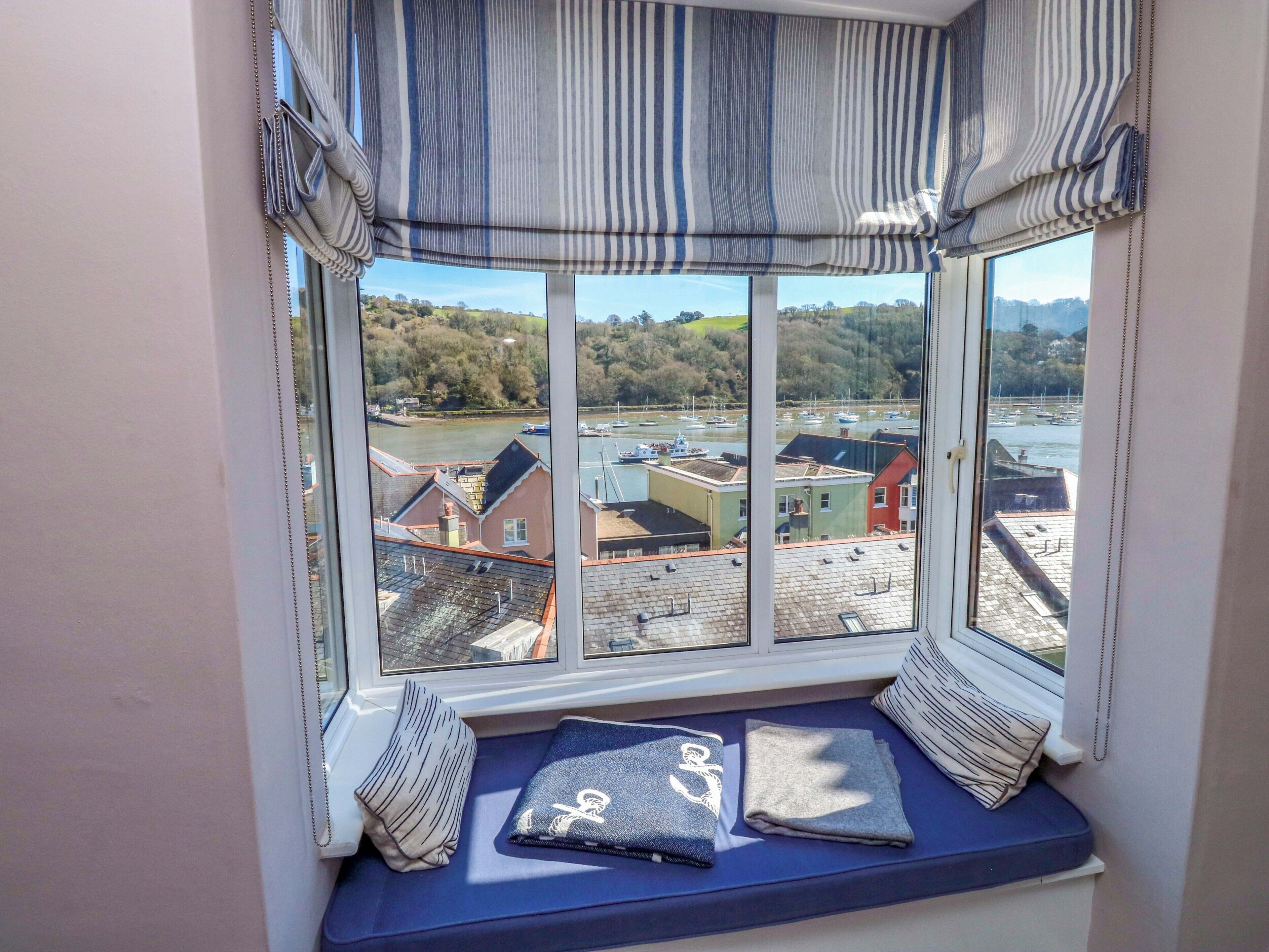 A bay window with a view of a harbor, a cushioned bench, and striped curtains.